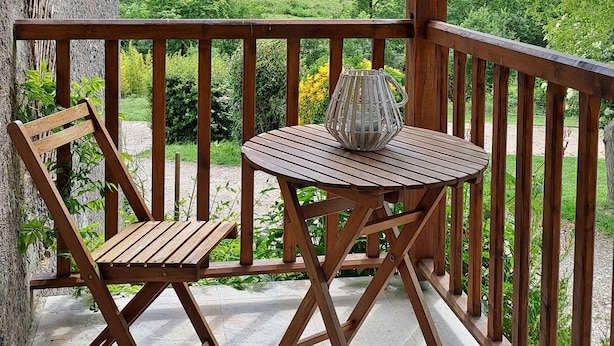 A wooden balcony with a table and two chairs, overlooking a green landscape with trees and a horse. - Gîte à la ferme de Palauqui, ideal for family vacations (Montjardin)