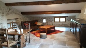 A cozy living room with a wooden table, a sofa, and a coffee table. There is a window with two panes and a stone wall. - Gîte à la ferme de Palauqui, ideal for family vacations (Montjardin)