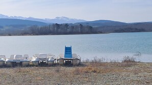 A row of small boats with the name "BALADO" on them, docked on a pebbly shore by a lake with mountains in the background. - Gîte à la ferme de Palauqui, ideal for family vacations (Montjardin)