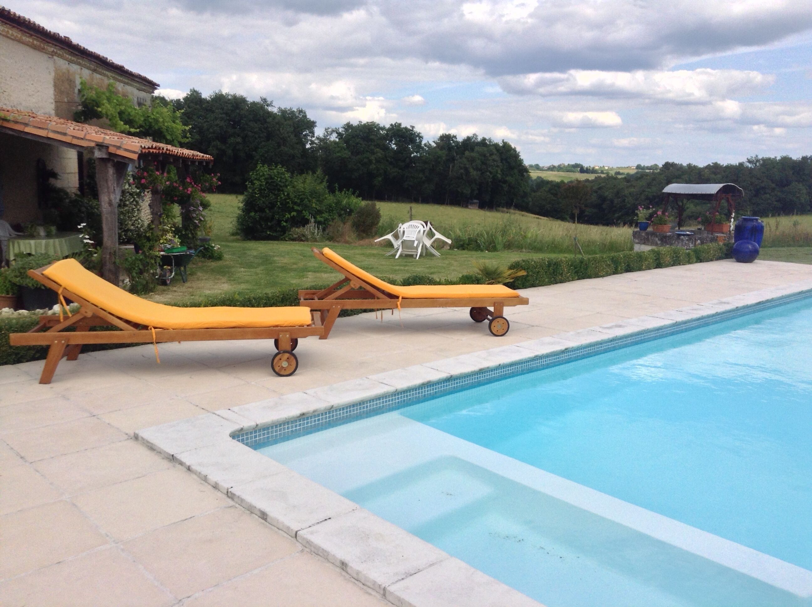 Une piscine avec deux chaises longues et un petit espace jardin aménagé avec une table et des chaises.