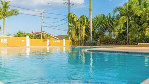 Une piscine à l’eau d’un bleu cristallin, entourée de palmiers et bordée d’un mur jaune.
