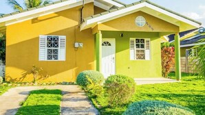 Un bâtiment jaune avec une porte et des fenêtres blanches, entouré d’une pelouse bien entretenue et de petits arbustes.