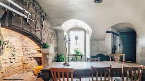 Un intérieur rustique avec un mur en pierre, des meubles en bois et une vue dégagée sur l’extérieur, visible à travers une porte en arc de cercle.