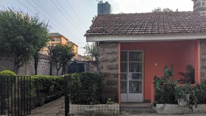 Een huis met een rode gevel, een pannendak en een stenen muur. Achtergrond toont een zwarte wateropslag, en een verharde oprit die naar de ingang leidt.