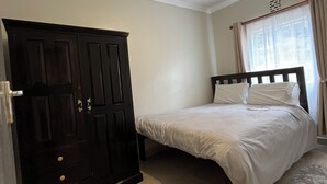 Een slaapkamer met een bed, een kledingkast, een plafondlamp en een raam met gordijnen.