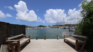 Un muelle de madera con bancos que conduce a una marina con barcos y un cielo despejado.