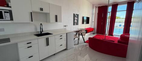 A modern kitchen with white cabinets, a black sink, and a dining area with a red sofa and table.