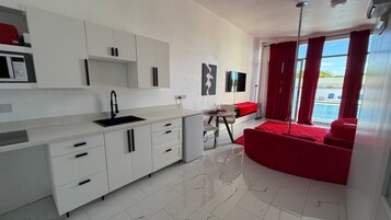 A modern kitchen with white cabinets, a black sink, and a dining area with a red sofa and table.