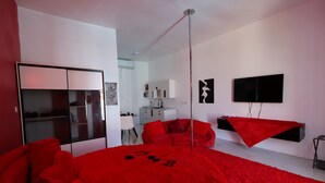 Un dormitorio moderno con una cama grande, un armario, un televisor y un sofá rojo.
