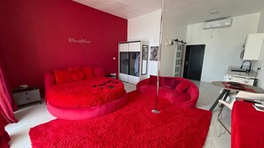 A room with a bed, a red sofa, a glass table, and a wardrobe. - PÀRIS Villas Honeymoon Suite (Gros Islet)