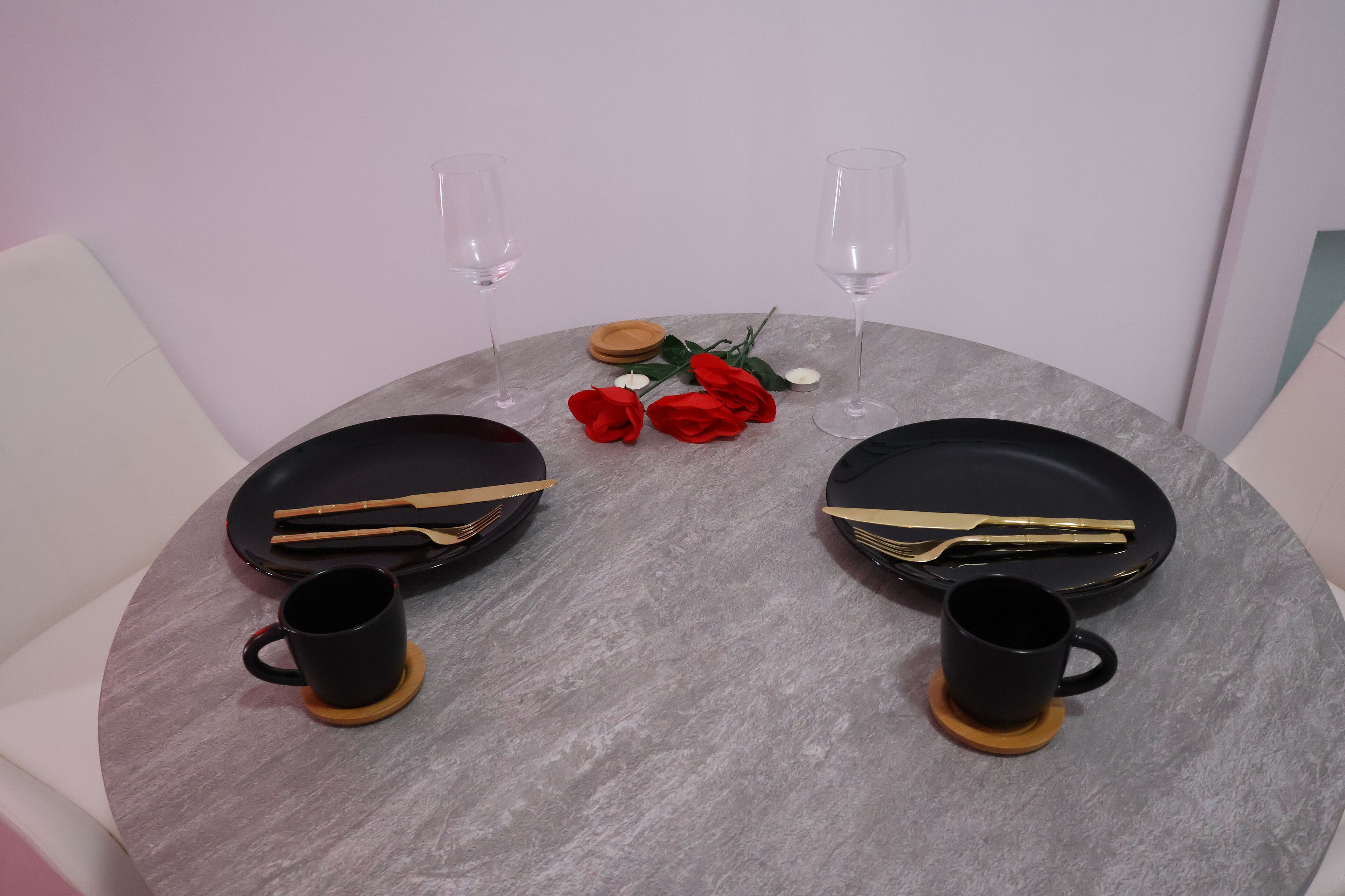 Une table de salle à manger ronde, avec deux assiettes noires, deux tasses noires et une paire de baguettes.