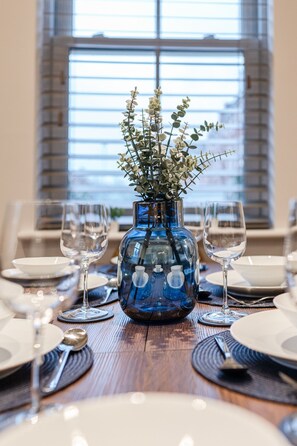 A dining table set with plates, glasses, and a blue vase with white flowers.
