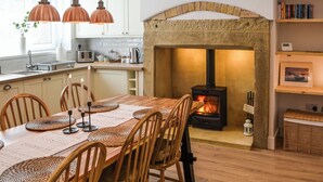 Une cuisine chaleureuse avec un poêle à bois, une table à manger en bois, des chaises et des luminaires suspendus.