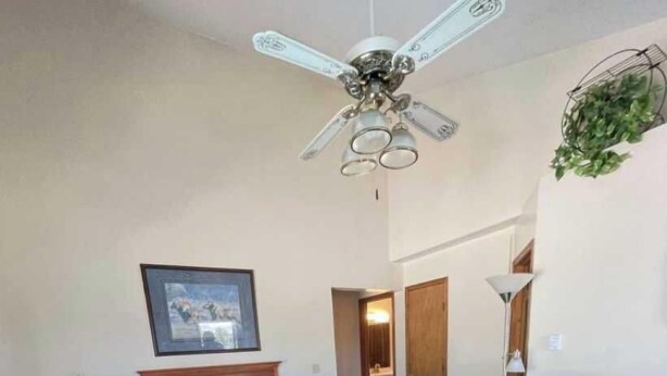 A hotel room with a bed, a wooden table, a brown leather chair, a ceiling fan, and a framed picture on the wall.