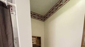 A small, clean bathroom with a toilet, a shower, and a shelf with toiletries.