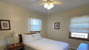 A bedroom with a bed, a nightstand, a ceiling fan, and two windows with blinds.