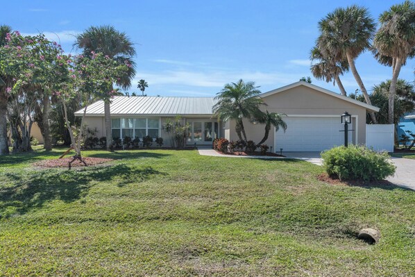 A single-story house with a garage, surrounded by a well-maintained lawn and palm trees.