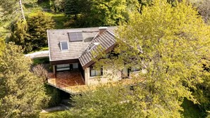 Een modern huis met een schuin dak, zonnepanelen en een grote boom op de voorgrond.