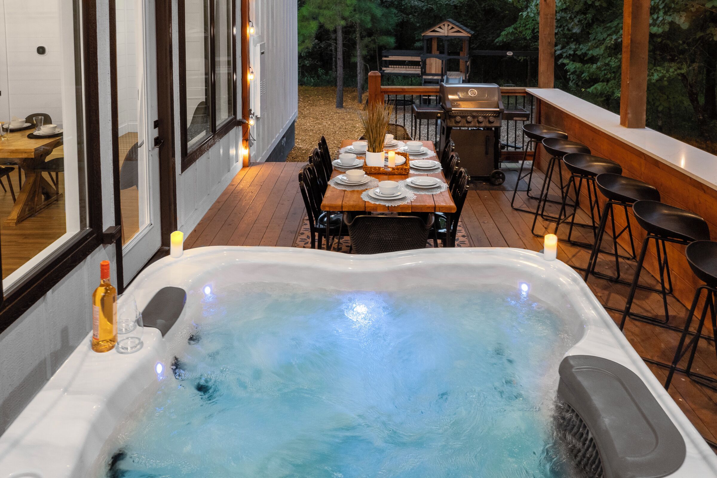 A hot tub with a wooden deck, a dining table with chairs, and a barbecue grill.