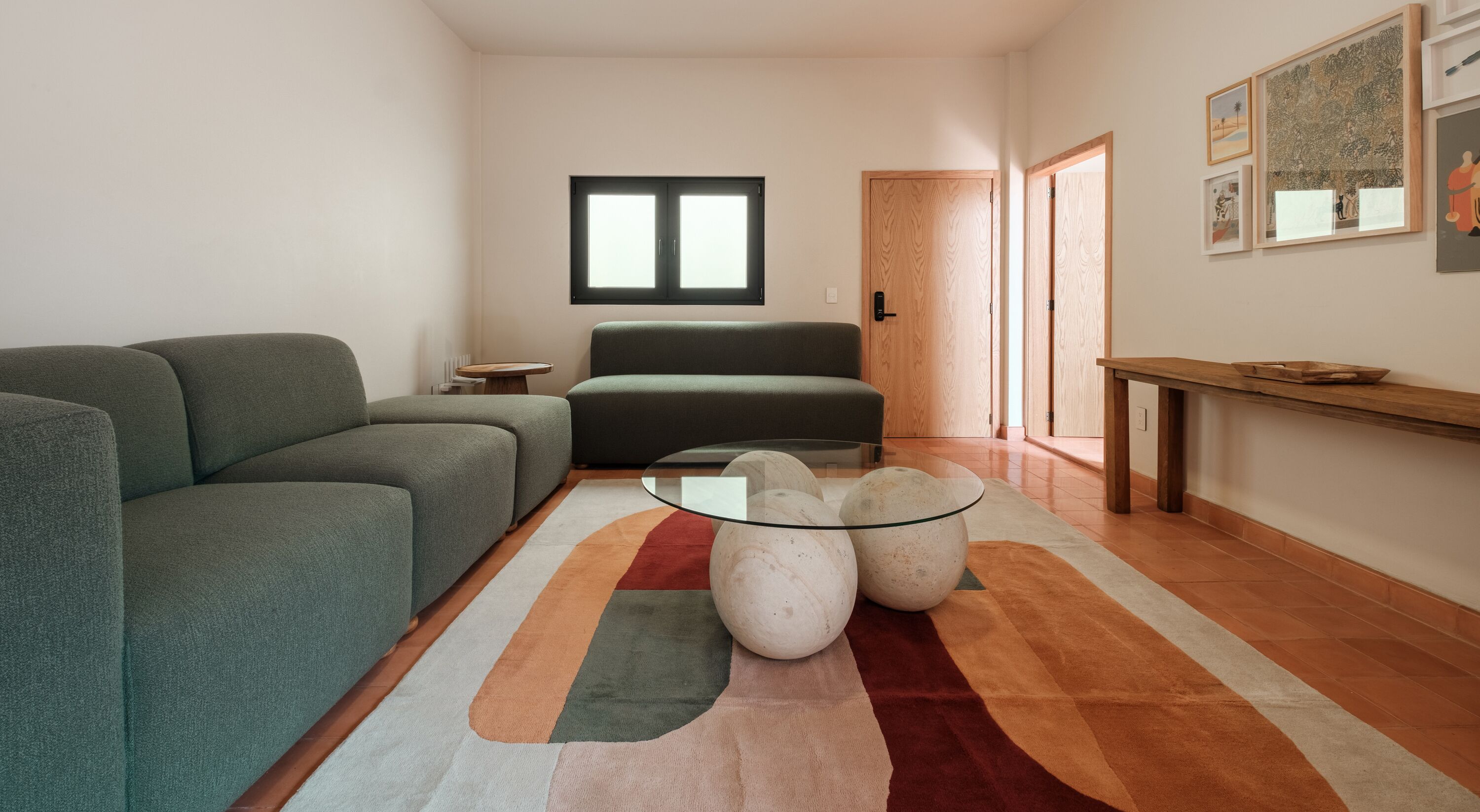 Un salon moderne avec un canapé vert, une table basse en verre ornée d’objets sphériques et un tapis aux couleurs vives.