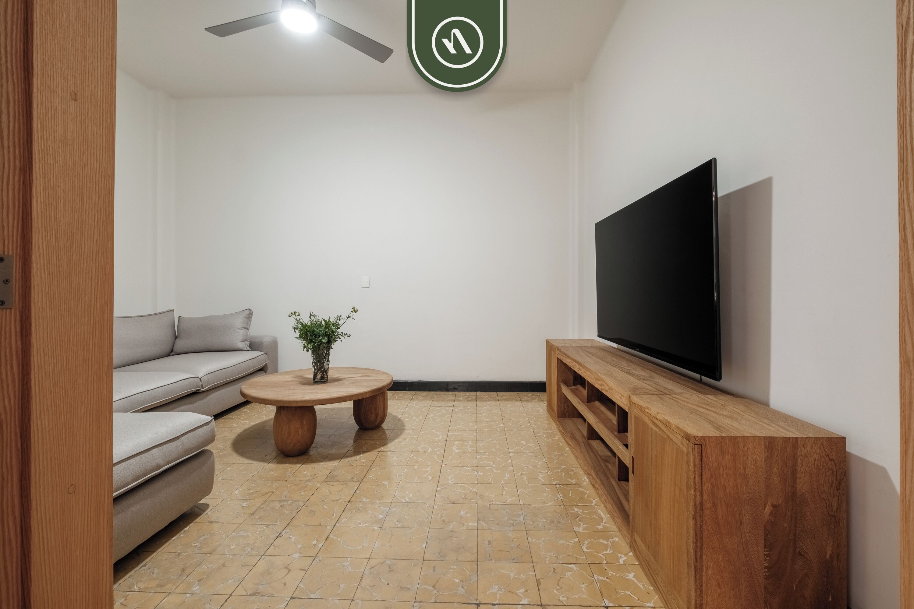 Una sala de estar moderna con un sofá gris, una mesa de centro de madera, un televisor de pantalla plana y un ventilador de techo.