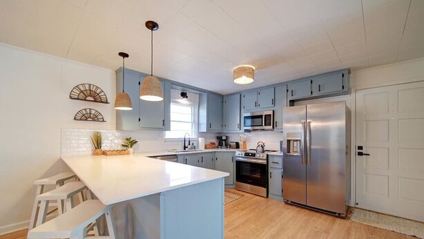 A modern kitchen with light blue cabinets, stainless steel appliances, and a central island with bar stools. - Cozy Riverside Cottage—Quiet—3-Beds—Fully Updated! (Belmont)