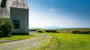 Une maison avec un chemin de gravier menant à une pelouse et offrant une vue sur la mer.