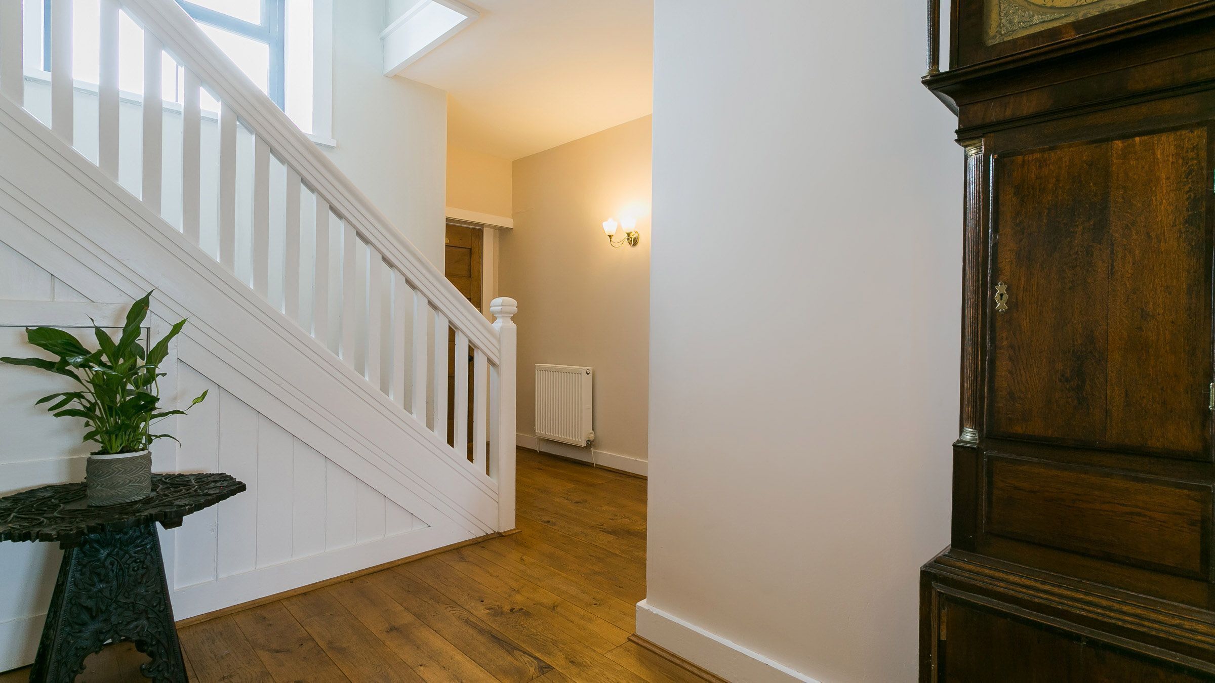 A staircase with white railings, a potted plant, and a wooden floor.