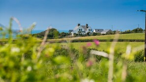 A house with a white exterior, surrounded by green fields and a clear blue sky.