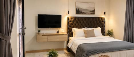 A modern hotel room with a large bed, a flat-screen TV, a bedside table with a plant, and a welcome sign.