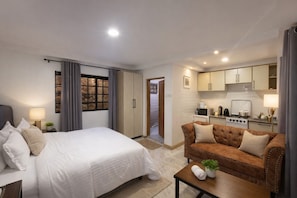 A hotel room with a bed, a sofa, a small table with a plant, and a kitchenette.