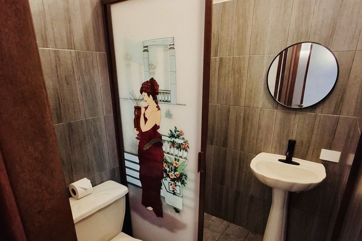 A bathroom with a toilet, a sink, and a decorative panel with a woman.
