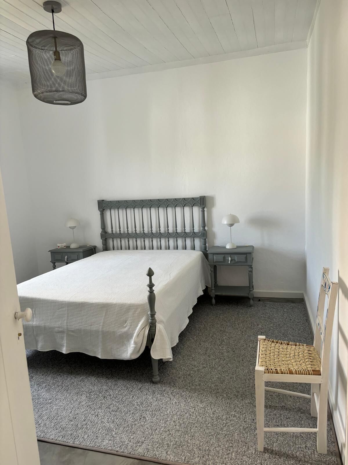 Ein Schlafzimmer mit einem Bett, zwei Nachttischen, einem Sessel und einer Pendelleuchte.