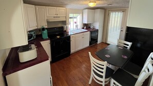 A compact kitchen with white cabinets, a black stove, and a dining table with chairs. - Retro Retreat! 2BR, 1 Bath Home with WiFi, AC in wonderful Bristol, VA (Bristol)