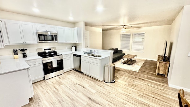 A compact kitchen with white cabinets, a microwave, stove, and sink. There's a small dining area with a table and chairs, and a ceiling fan.