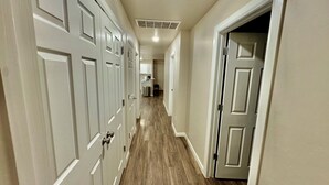 A hallway with multiple white doors, a light-colored floor, and a ceiling vent.