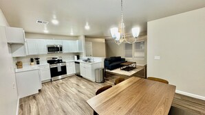 A compact kitchen with white cabinets, a microwave, stove, and a small island with a sink. There is a dining table with chairs and a dark-colored sofa in the living area.
