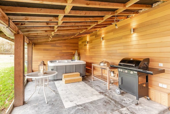 Un espacio exterior techado con un jacuzzi, una parrilla y una mesa con sillas.