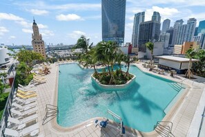 A rooftop pool with palm trees, lounge chairs, and a cityscape view.