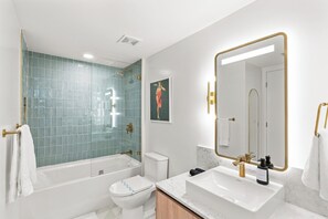 A modern bathroom with a glass-enclosed shower, a white toilet, a sink with a gold faucet, and a large mirror with a gold frame.