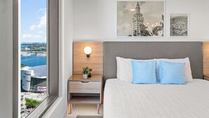 A hotel room with a large bed, a nightstand with a lamp, and a view of a cityscape.