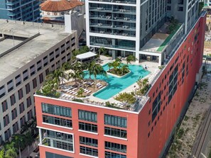 A rooftop pool with sun loungers and palm trees, surrounded by modern buildings.