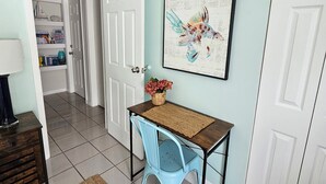 A room with a light blue wall, a white door, a wooden table with a woven placemat, a blue chair, a framed picture, and a small basket with flowers. - #1. Peaceful Private Room Near FLL Airport (Sunrise)