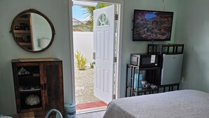 A bedroom with a bed, a television, a desk with a chair, a wardrobe, and a door leading outside. - #1. Peaceful Private Room Near FLL Airport (Sunrise)