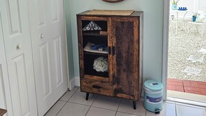 A room with a white door, a wooden cabinet with shelves, a round mirror, and a blue trash bin. - #1. Peaceful Private Room Near FLL Airport (Sunrise)
