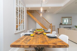A dining area with a wooden table set for breakfast, white chairs, and a staircase in the background. - Heatherleigh, Carbis Bay – Sleeps 8 – Sea Views – Dog-Friendly - On-Site Parking (Carbis Bay)