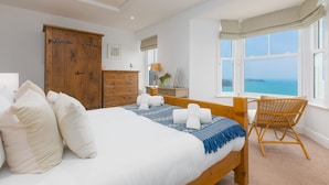A bedroom with a large bed, wooden wardrobe, and a view of the sea through a window. - Heatherleigh, Carbis Bay – Sleeps 8 – Sea Views – Dog-Friendly - On-Site Parking (Carbis Bay)