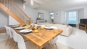 A dining area with a wooden table, white chairs, and a staircase. - Heatherleigh, Carbis Bay – Sleeps 8 – Sea Views – Dog-Friendly - On-Site Parking (Carbis Bay)