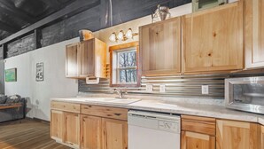 Une cuisine avec des meubles en bois, un lave-vaisselle, un four à micro-ondes et une fenêtre donnant sur les arbres.