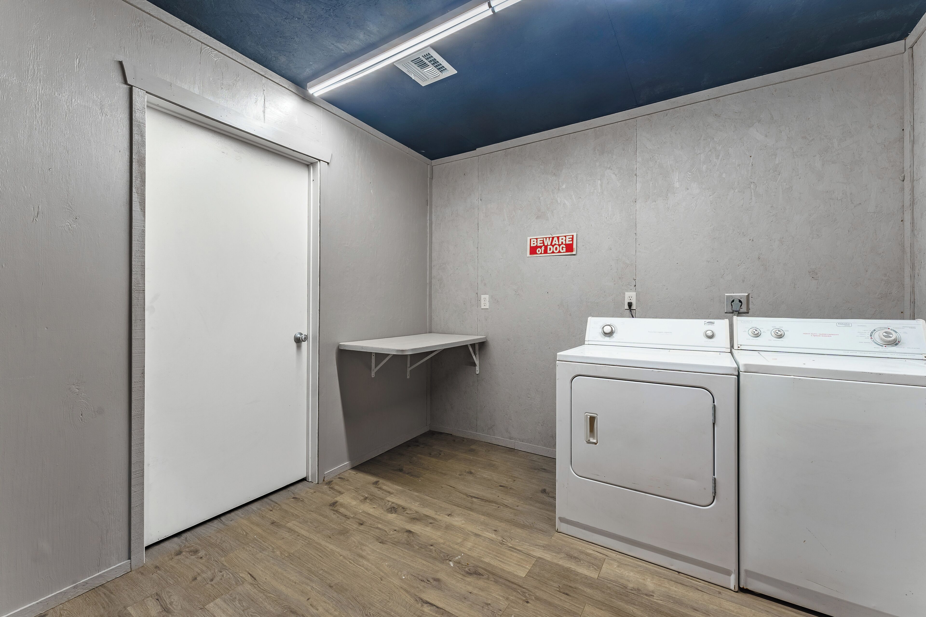 A laundry room with a white door, a shelf, and two white washing machines.